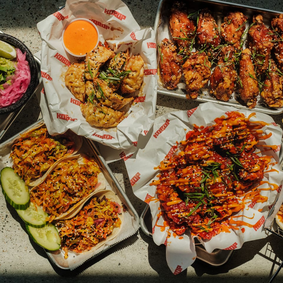 Overhead spread of Korean fried chicken, dumplings, loaded fries, tacos, guacamole, pickled vegetables, and dipping sauce.