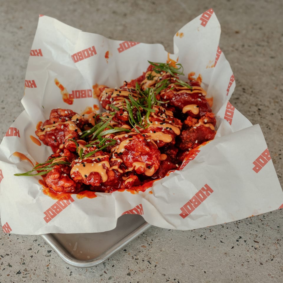 Crispy Korean-style chicken pieces coated in red sauce, drizzled with orange sauce, and topped with sesame seeds and green onions.